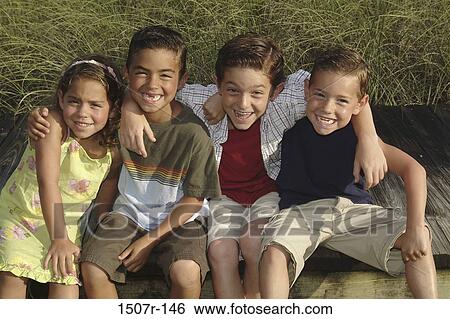 Stock Photograph - Portrait of three boys and a girl sitting on a lawn smiling. Fotosearch