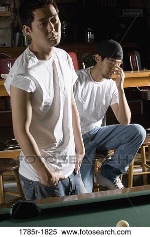 Stock Photography - Portrait of two men in jeans and t-shirts in front of billiards table. Fotosearch