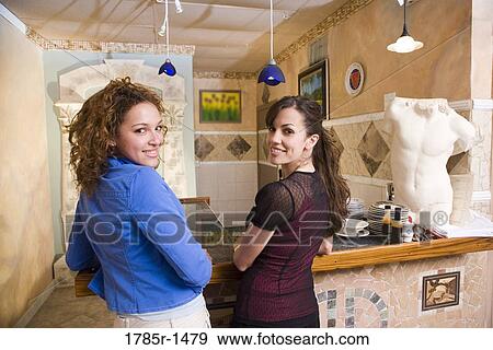 Stock Photo - Portrait of two smiling young Hispanic women standing at a bar in a restaurant. Fotosearch