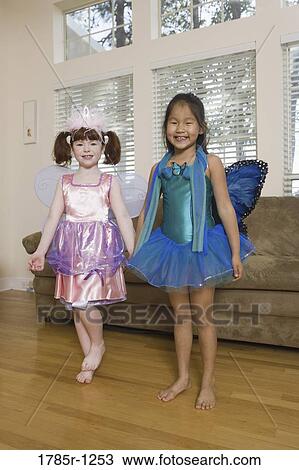 Stock Image - Portrait of two young girls in costumes dancing in living room. Fotosearch