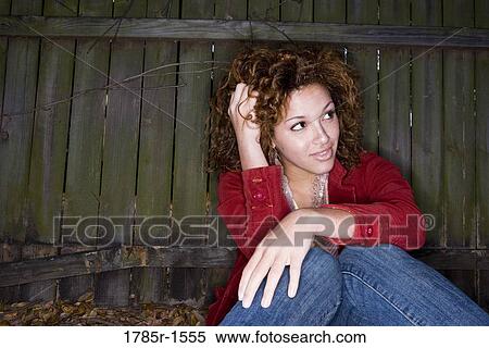 Portrait of young woman with hands running through her hair, sitting against a wooden fence View Large Photo Image Stock Photography - Portrait of young woman with hands running through her hair, sitting against a wooden fence. Fotosearch