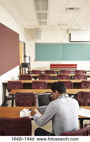 Rear view of a college student sitting in a lecture hall in front of a laptop View Large Photo Image Stock Image - Rear view of a college student sitting in a lecture hall in front of a laptop. Fotosearch