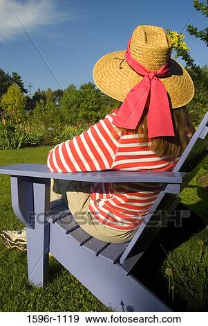 Rear view of a mid adult woman sitting on an adirondack chair in a garden View Large Photo Image Stock Photo - Rear view of a mid adult woman sitting on an adirondack chair in a garden. Fotosearch