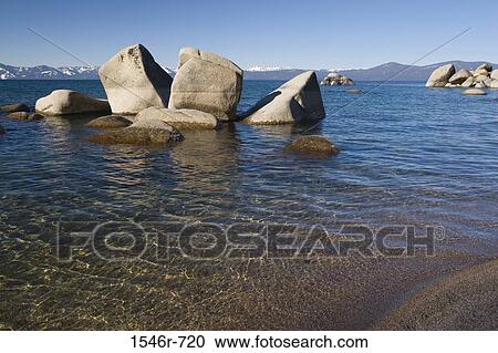 Stock Image - Rock formations in a lake with mountains in the background, Lake Tahoe, Nevada, USA. Fotosearch