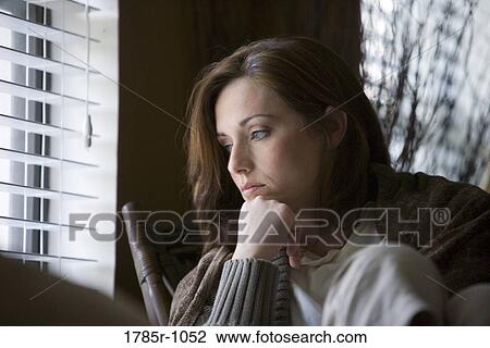 Sad young woman sitting on chair by window View Large Photo Image Stock Image - Sad young woman sitting on chair by window. Fotosearch