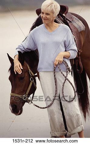 Stock Image - Senior woman standing with a horse. Fotosearch