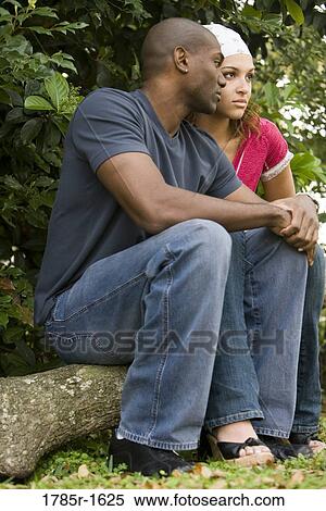 Serious young multi-ethnic couple sitting on a log View Large Photo Image Stock Photography - Serious young multi-ethnic couple sitting on a log. Fotosearch