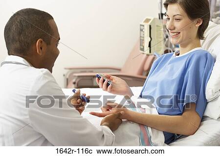 Stock Image - Side profile of a male doctor taking a blood sample from a female patient's finger. Fotosearch