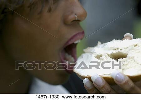 Side profile of a young woman eating a bagel View Large Photo Image Stock Image - Side profile of a young woman eating a bagel. Fotosearch