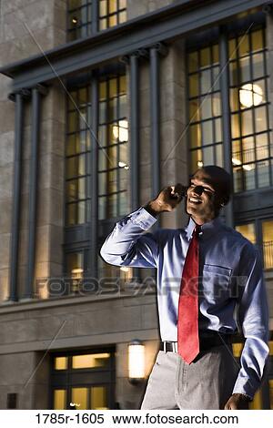 Smiling young businessman talking on mobile phone at dusk in front of building View Large Photo Image Stock Photography - Smiling young businessman talking on mobile phone at dusk in front of building. Fotosearch