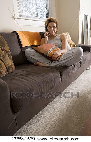 Smiling young woman sitting on sofa talking on cordless phone View Large Photo Image Stock Photo - Smiling young woman sitting on sofa talking on cordless phone. Fotosearch