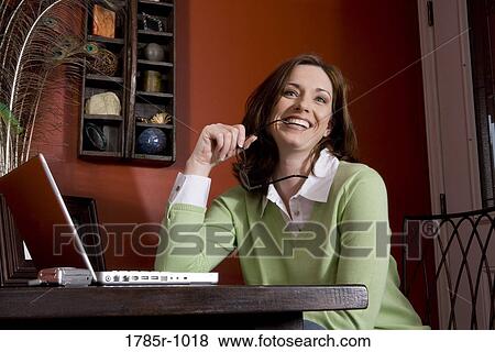 Stock Photo - Smiling young woman sitting with laptop at desk. Fotosearch