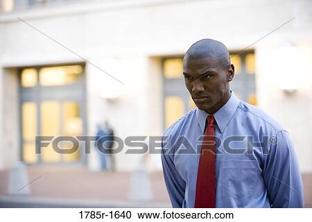 Stern looking young businessman standing outside a building View Large Photo Image Stock Image - Stern looking young businessman standing outside a building. Fotosearch