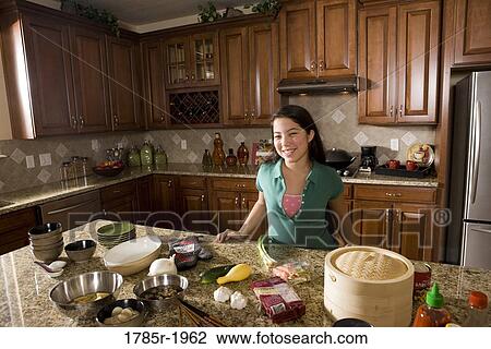 Stock Image - Teenage girl in kitchen with ingredients for Asian-style dish. Fotosearch