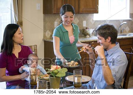 Picture - Teenage girl serving food to her family at home. Fotosearch