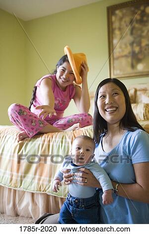 Teenage girl sitting on bed with mother and baby brother on floor View Large Photo Image Stock Image - Teenage girl sitting on bed with mother and baby brother on floor. Fotosearch