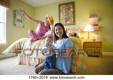 Stock Photo - Teenage girl sitting on bed with mother and baby brother on floor. Fotosearch