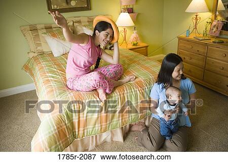Teenage girl sitting on bed with mother and baby brother on floor View Large Photo Image Stock Photo - Teenage girl sitting on bed with mother and baby brother on floor. Fotosearch