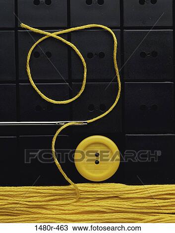 Stock Image - Thread through the eye of a needle near a button. Fotosearch