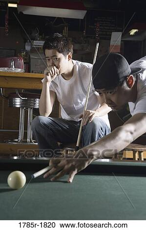 Stock Image - Two Asian men in jeans and t-shirts playing billiards. Fotosearch
