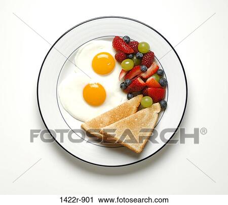 Stock Image - Two fried eggs, two slices of toast and fruit salad on plate. Fotosearch