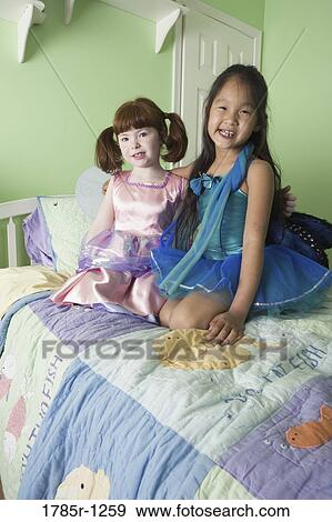Two young Asian girls in costumes sitting on bed View Large Photo Image Stock Photo - Two young Asian girls in costumes sitting on bed. Fotosearch