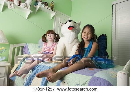 Two young girls in costumes sitting on bed with large stuffed animal View Large Photo Image Stock Photo - Two young girls in costumes sitting on bed with large stuffed animal. Fotosearch