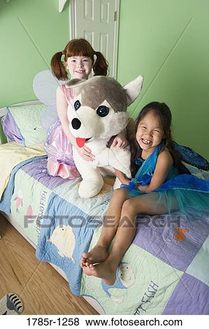 Two young girls in costumes sitting on bed with large stuffed animal View Large Photo Image Stock Photo - Two young girls in costumes sitting on bed with large stuffed animal. Fotosearch