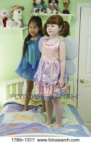 Two young girls in costumes standing on bed View Large Photo Image Stock Photo - Two young girls in costumes standing on bed. Fotosearch