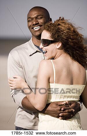 Stock Image - View of a happy young couple embracing on beach. Fotosearch