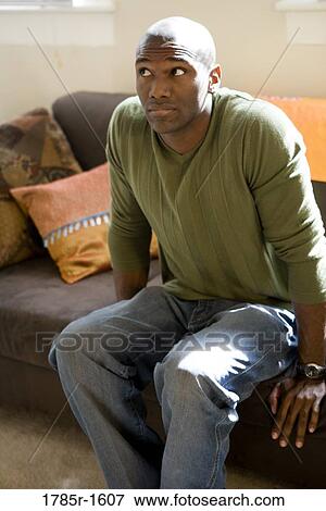 Stock Photo - View of a nervous and contemplative young man sitting on sofa. Fotosearch