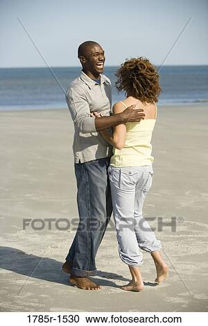 Stock Image - View of a young couple embracing and frolicking on beach. Fotosearch