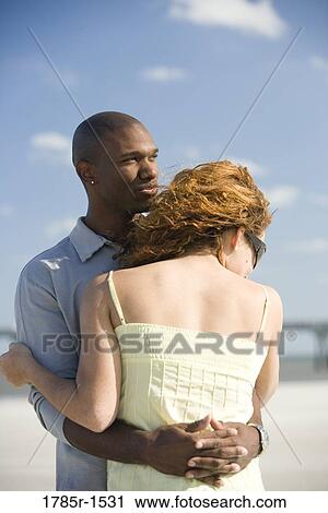 Stock Image - View of a young couple embracing on beach. Fotosearch