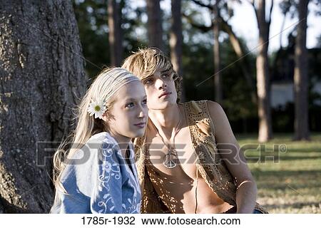 Stock Image - View of a young couple in vintage 1960's hippie costumes sitting in a park. Fotosearch