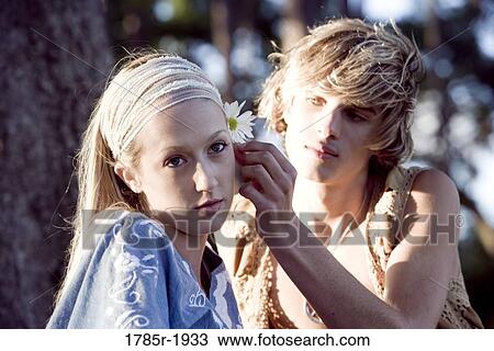 Stock Image - View of a young couple in vintage 1960's hippie, putting flower behind ear. Fotosearch