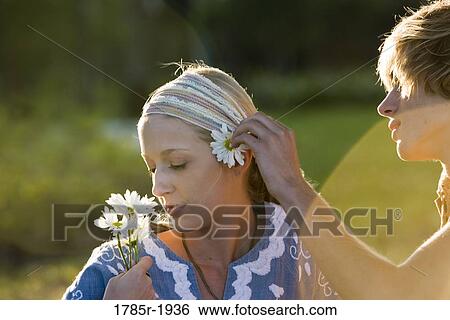 Stock Photograph - View of a young couple in vintage 1960's hippie, putting flower behind ear. Fotosearch