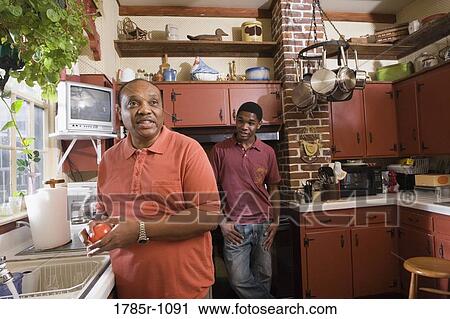 Stock Image - View of father and son conversing in kitchen. Fotosearch