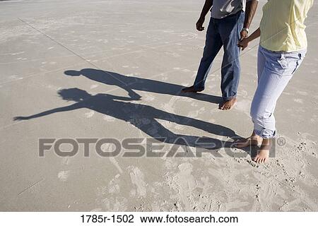 Stock Image - View of lower portion of romantic young couple standing on beach. Fotosearch