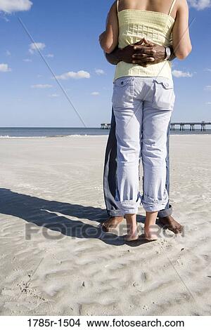 View of the back of a young woman embracing a man while standing on beach View Large Photo Image Picture - View of the back of a young woman embracing a man while standing on beach. Fotosearch