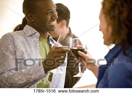 Stock Photograph - View of young couple socializing in a crowded bar while holding wineglasses. Fotosearch