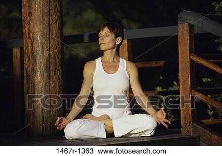 Stock Image - Woman sitting outdoors meditating. Fotosearch