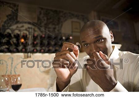Stock Image - Young African American man nervously holding and looking at an engagement ring. Fotosearch