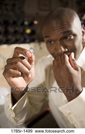 Stock Photo - Young African American man nervously holding and looking at an engagement ring. Fotosearch