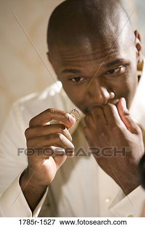 Stock Photo - Young African American man nervously holding and looking at an engagement ring. Fotosearch
