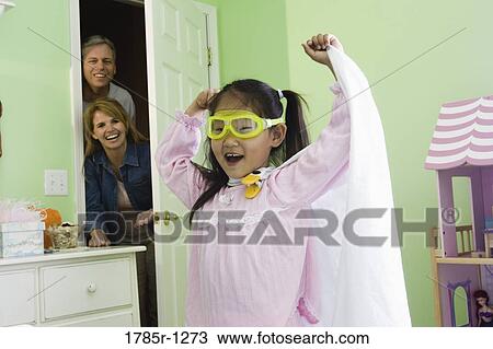 Stock Image - Young Asian girl in super-hero costume with parents watching. Fotosearch