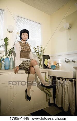Stock Photo - Young Asian woman leaning against countertop in apartment kitchen. Fotosearch