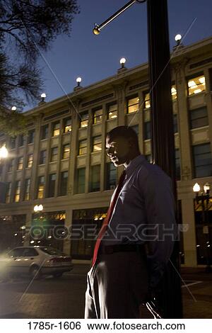 Young businessman leaning on pole at dusk, with building in the background View Large Photo Image Stock Photograph - Young businessman leaning on pole at dusk, with building in the background. Fotosearch
