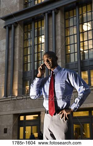 Young businessman talking on mobile phone at dusk, with building in background View Large Photo Image Picture - Young businessman talking on mobile phone at dusk, with building in background. Fotosearch