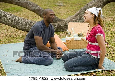 Young couple conversing while sitting on a picnic blanket View Large Photo Image Stock Image - Young couple conversing while sitting on a picnic blanket. Fotosearch