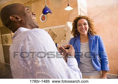 Stock Photography - Young couple holding wineglasses laughing and socializing. Fotosearch